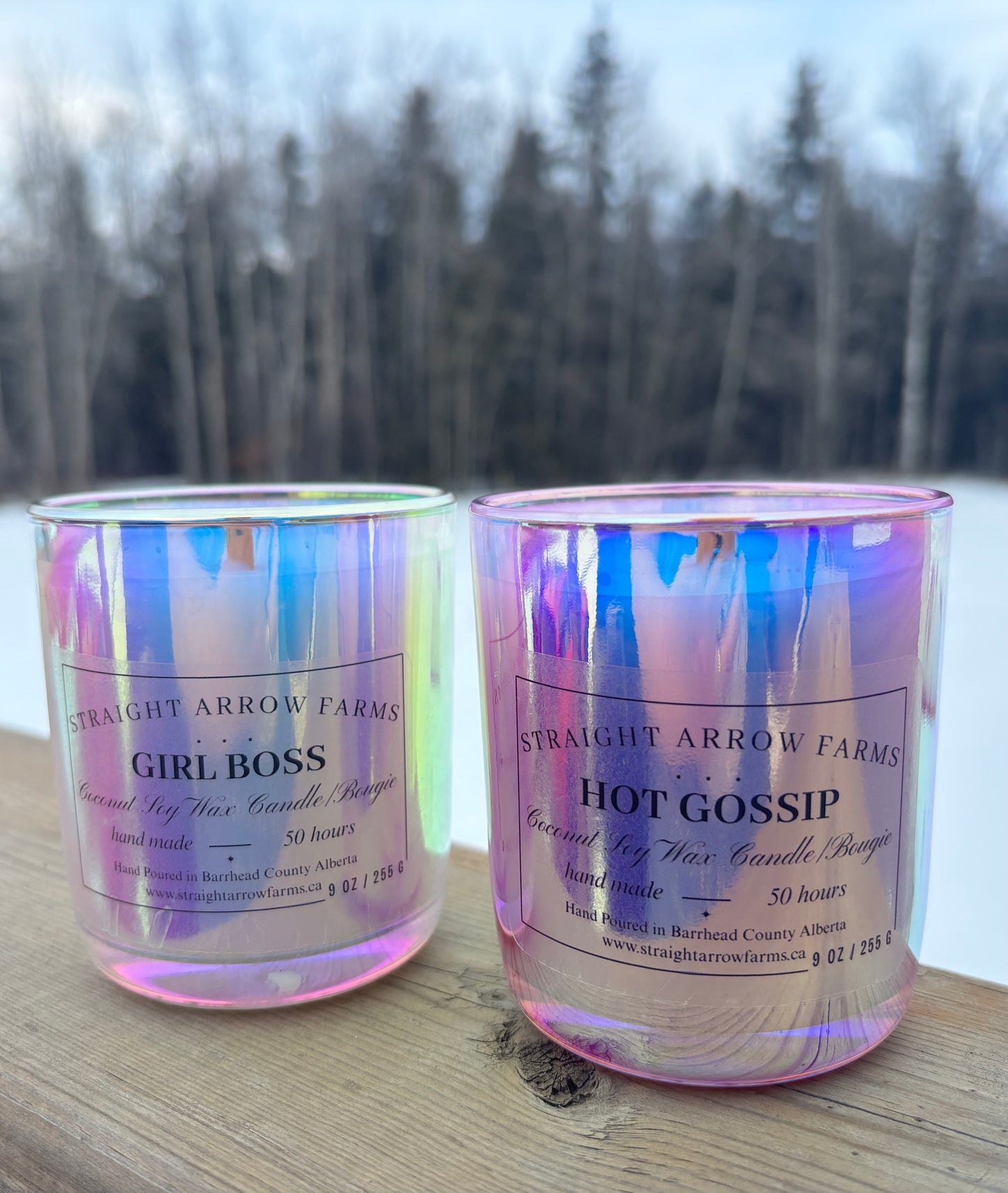Two iridescent candles with labels on a wooden surface with a blurred natural background