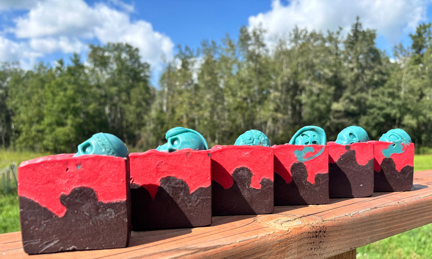 Straight arrow farms goat milk soap, scented in lost Cherry fragrance in a Halloween themed bar, layered in red and black with a green skull embed on top.