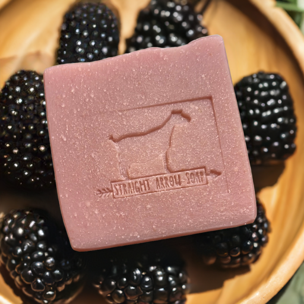 Blackberry Sage Goat Milk Soap resting on fresh blackberries, showcasing its creamy texture and natural ingredients.