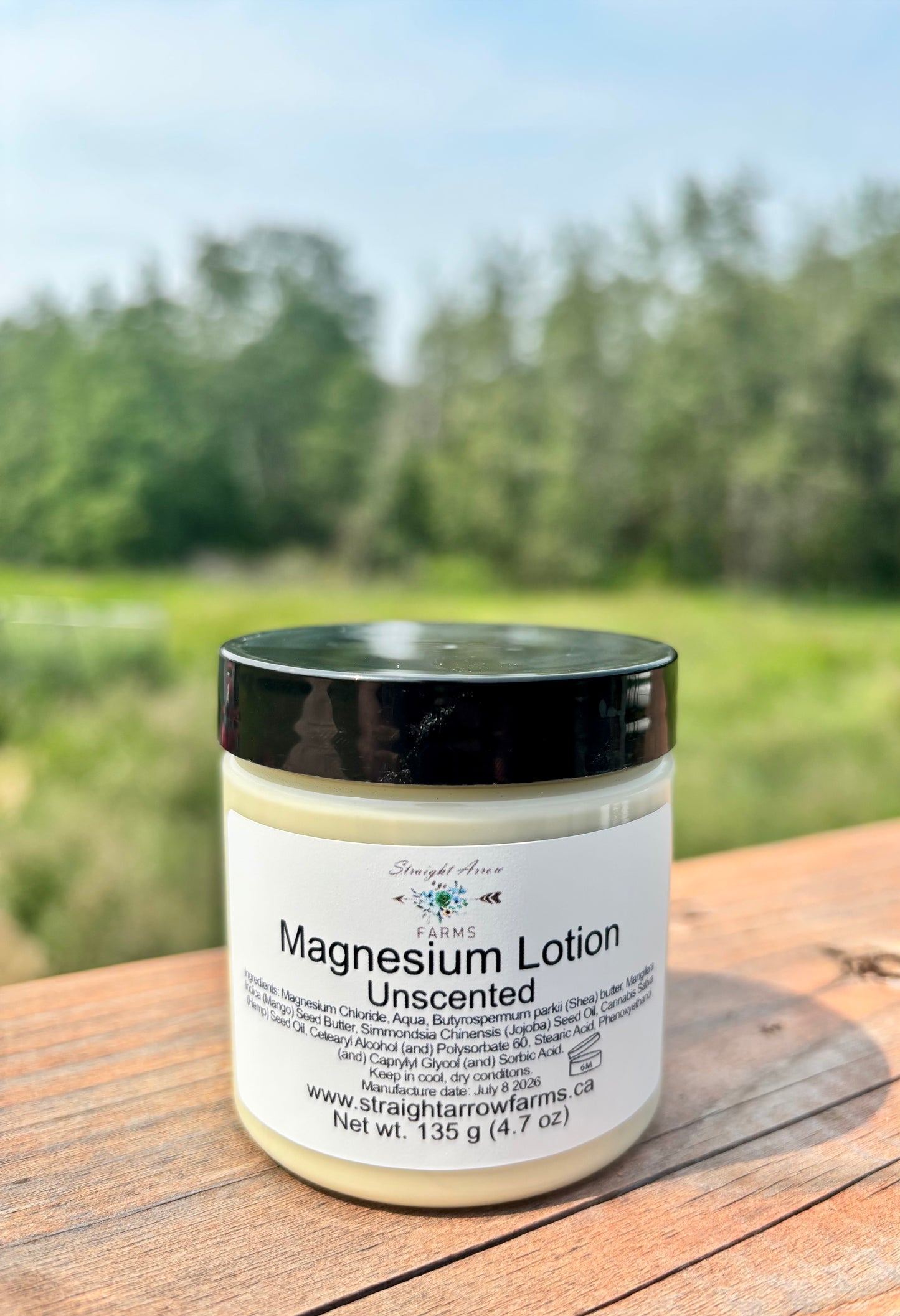 Straight Arrow Farms Magnesium Lotion Unscented, 135g jar with black lid, photographed outdoors on a wooden surface with a green field background