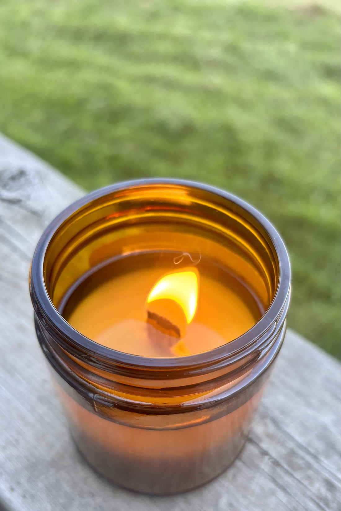 A lit wood wick candle in a glass jar, with the flame and melted wax visible