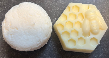 Hair Shampoo bar next to a hexagonal honeycomb-shaped hair conditioner bar on a dark surface. 
