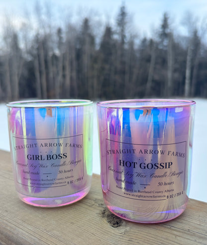 Two iridescent candles with labels on a wooden surface with a blurred natural background