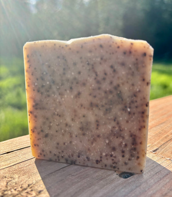 Bar of soap with coffee grounds exfoliant on a wooden surface with a blurred natural background