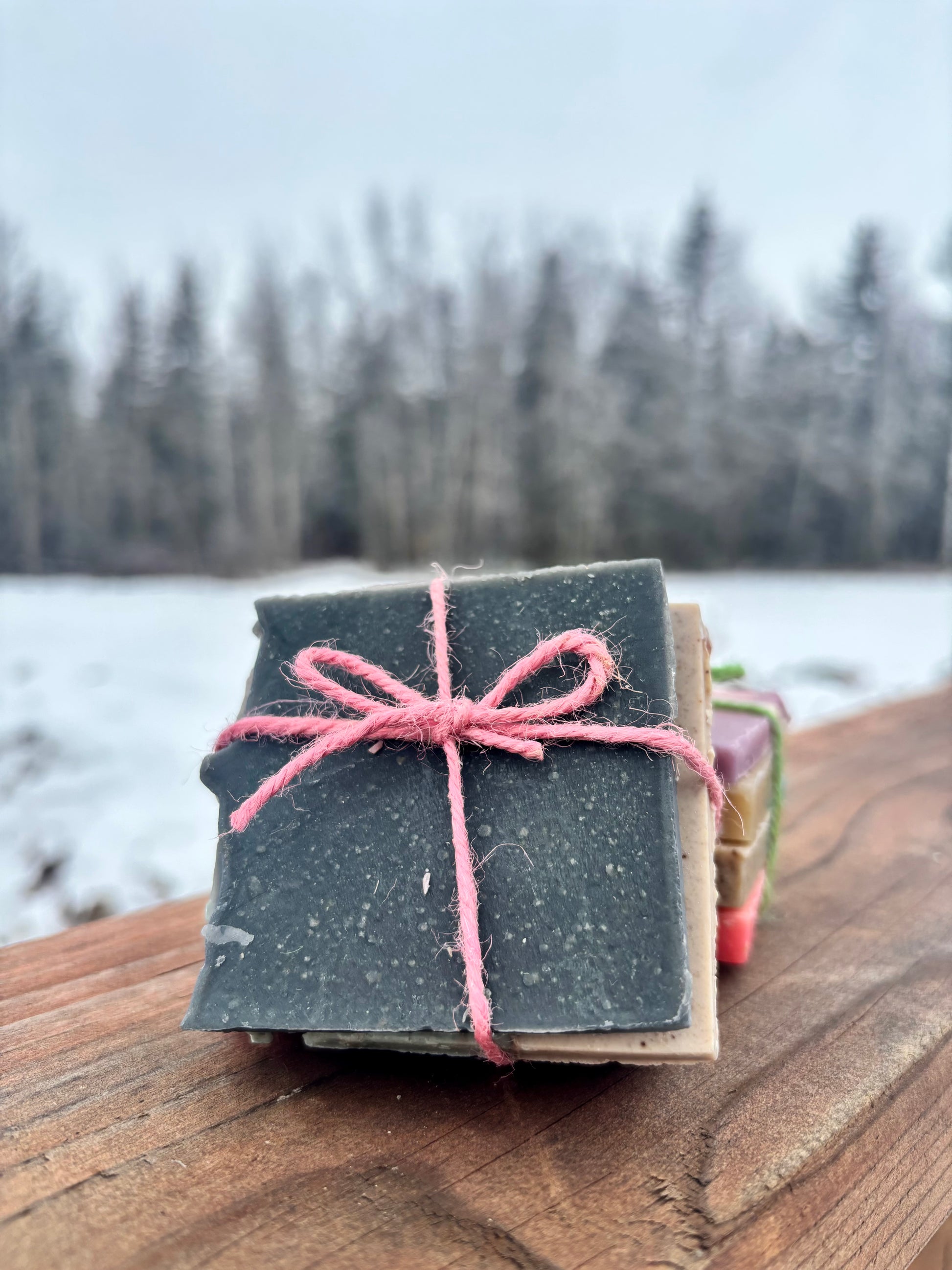 Stack of soap bars tied with pink string on a wooden surface with a lake and trees in the background