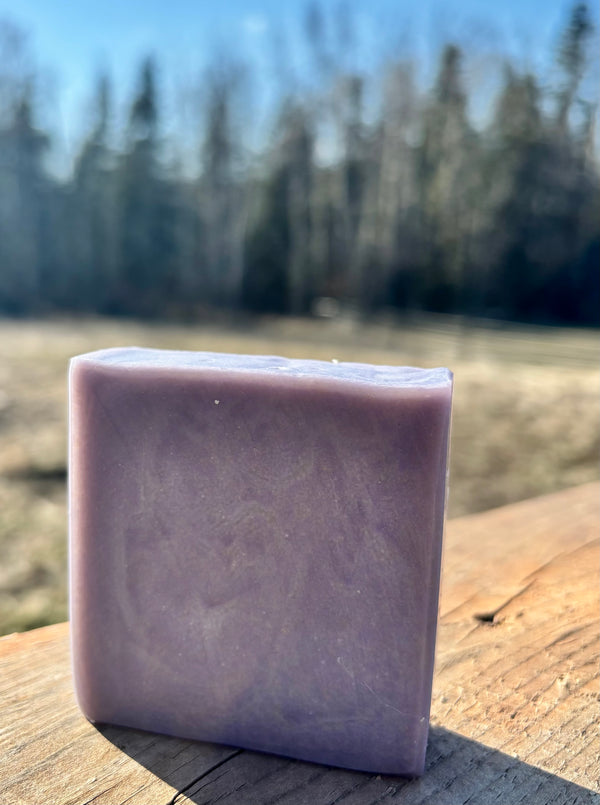 Purple soap bar on a wooden surface with a blurred natural background