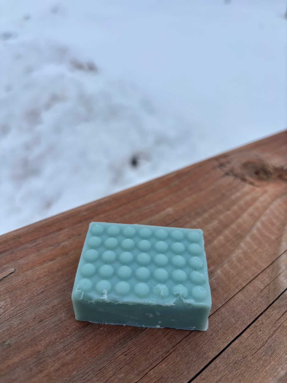 Green bar of soap with a textured surface on a wooden surface.
