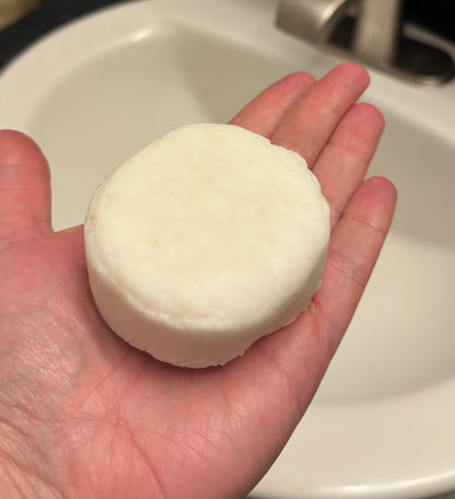 White shampoo bar held in a hand with a sink in the background