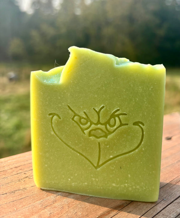 Green soap bar with a face design on a wooden surface outdoors