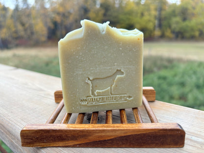 Bar of soap with a goat silhouette on a wooden soap dish against a natural background