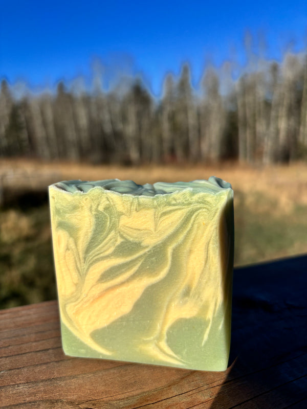 Green and white swirled soap bar on a wooden surface with a blurred natural background