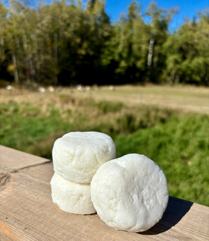 Three white spherical shampoo bars on a wooden surface with a natural background of trees and grass.