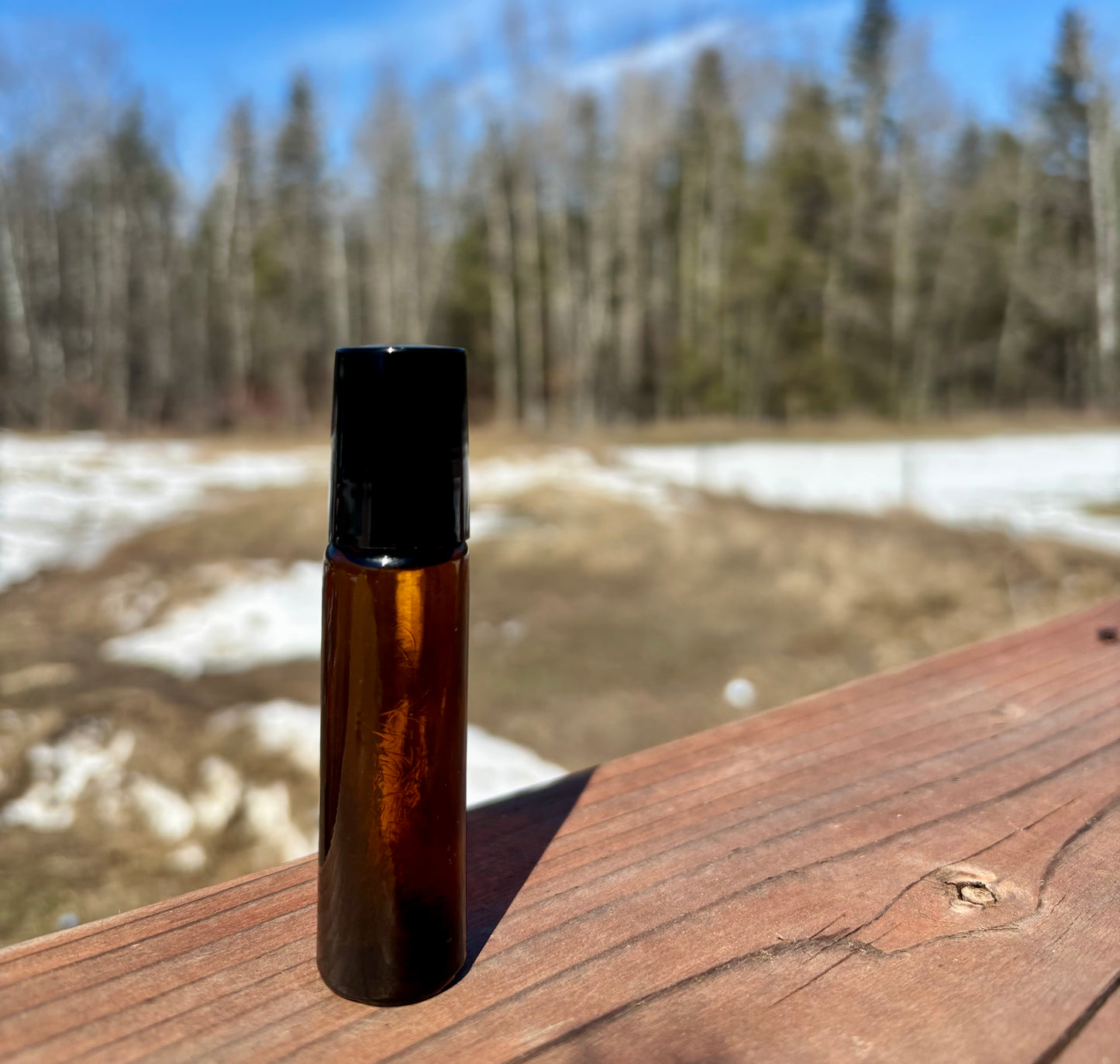 Brown rollerball bottle with black cap on a wooden surface with a forest background