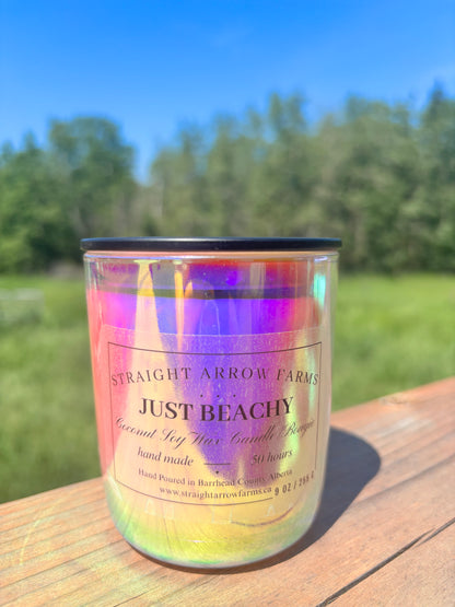 Candle labeled 'Just Beachy' on a wooden surface with a blurred natural background