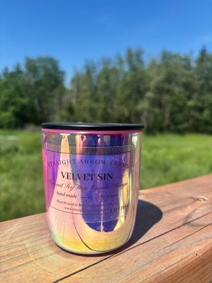 Candle scented in Velvet Sin in a iridescent container with 'Straight Arrow Farms' label on a wooden surface with a natural background