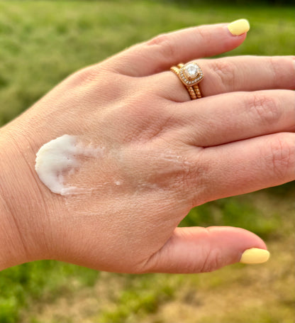 Whipped grass-fed tallow cream being applied to the back of a hand, showing creamy white texture, outdoors on a farm