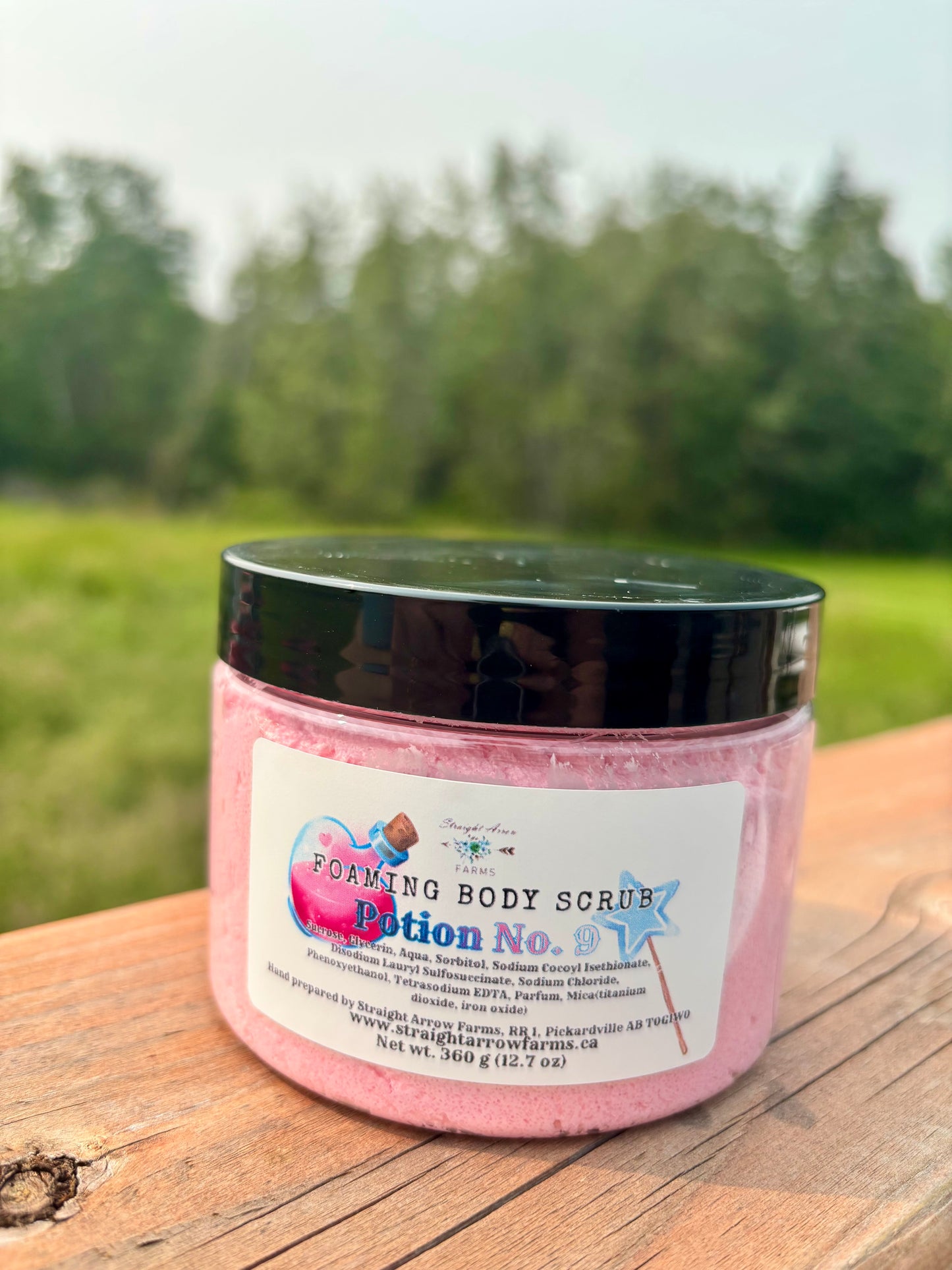 Straight Arrow Farms Foaming Body Scrub Potion No. 9, 360g jar with black lid and potion bottle label art, pink sugar scrub visible through jar, photographed outdoors on a wooden surface