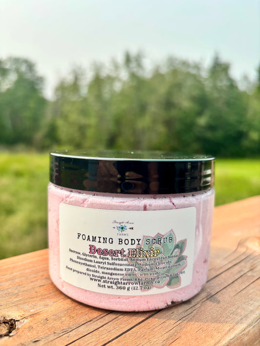 Straight Arrow Farms Foaming Body Scrub Desert Elixir, 360g jar with black lid and succulent label art, photographed outdoors on a wooden surface with a green field background
