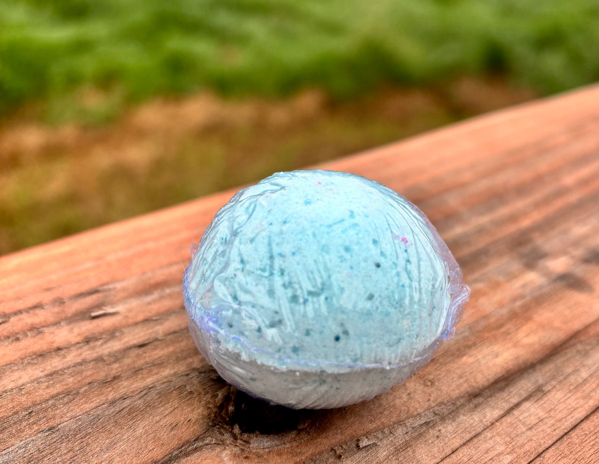 A blue bath bomb, resting on a wooden deck with a blurred green garden background.