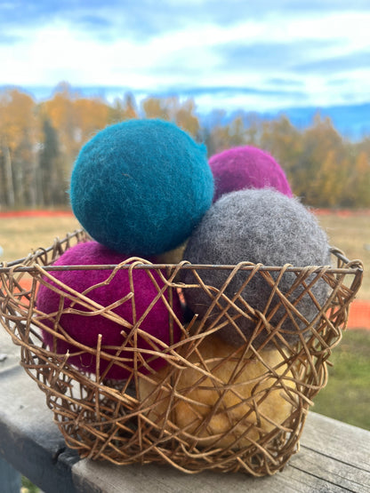 A basket containing multicolored wool dryer balls displayed outdoors with a scenic background.